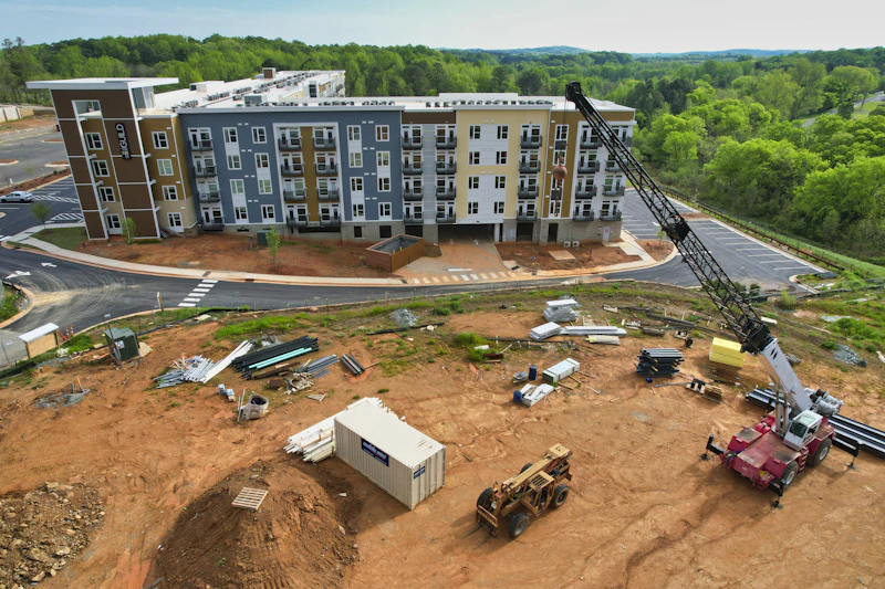 Canteiro de obras com edifício residencial ao fundo e equipamentos pesados